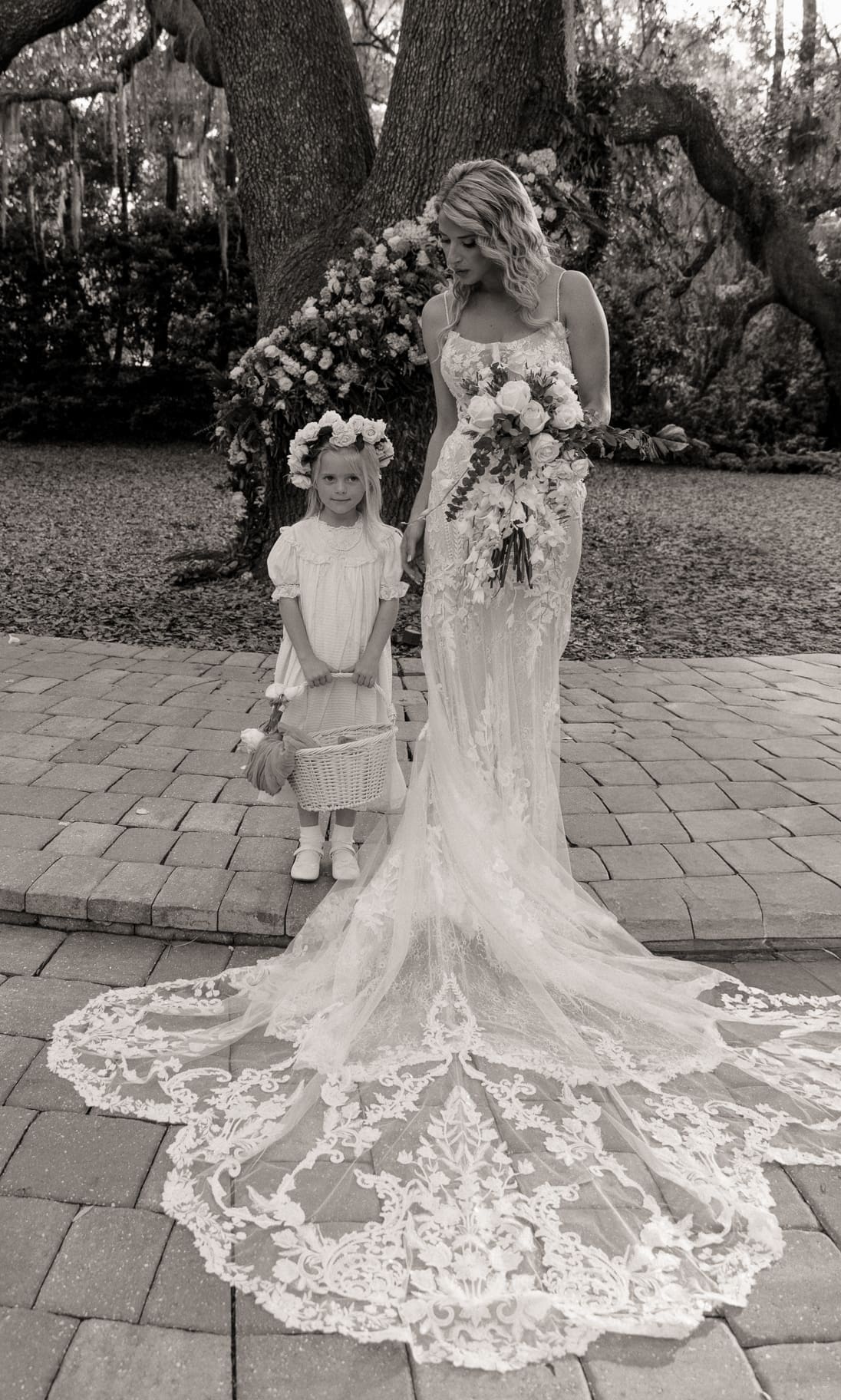 Bride standing with flower girl in front of large live oak.