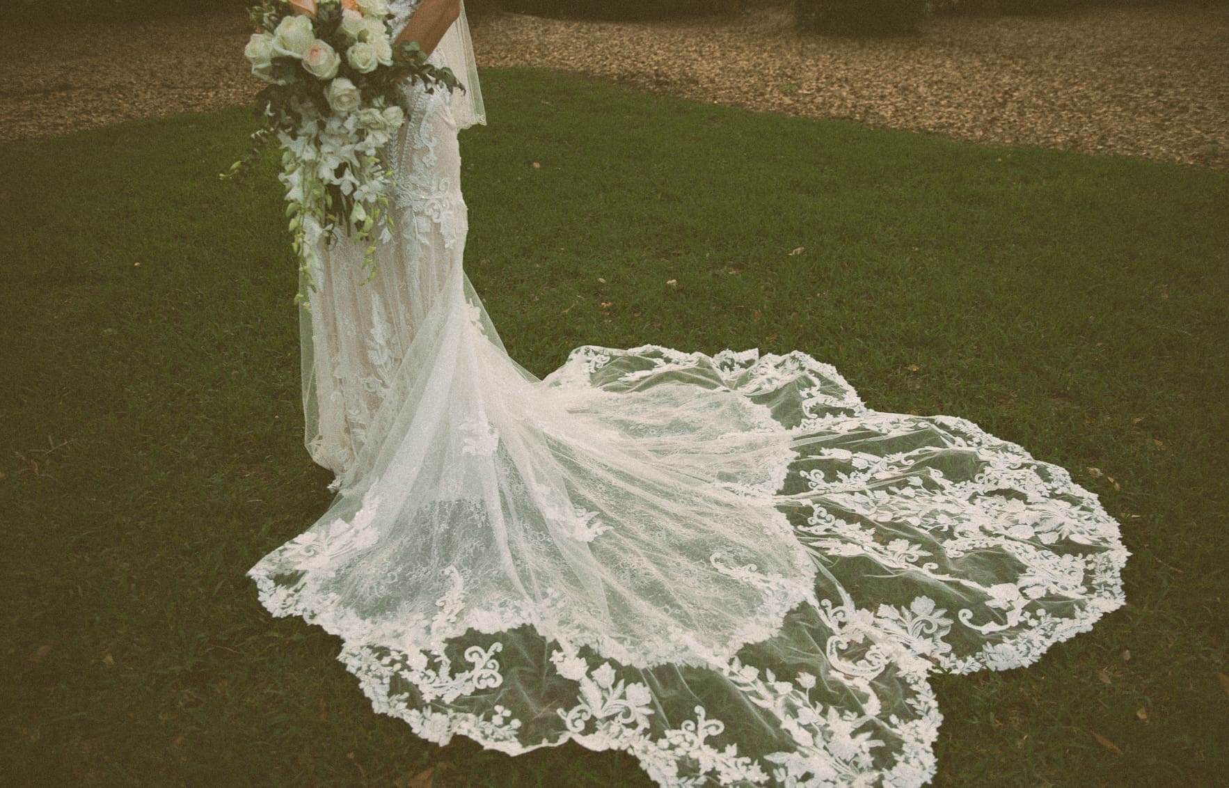 Close-up detail of bride's lace wedding gown train on the grass. 