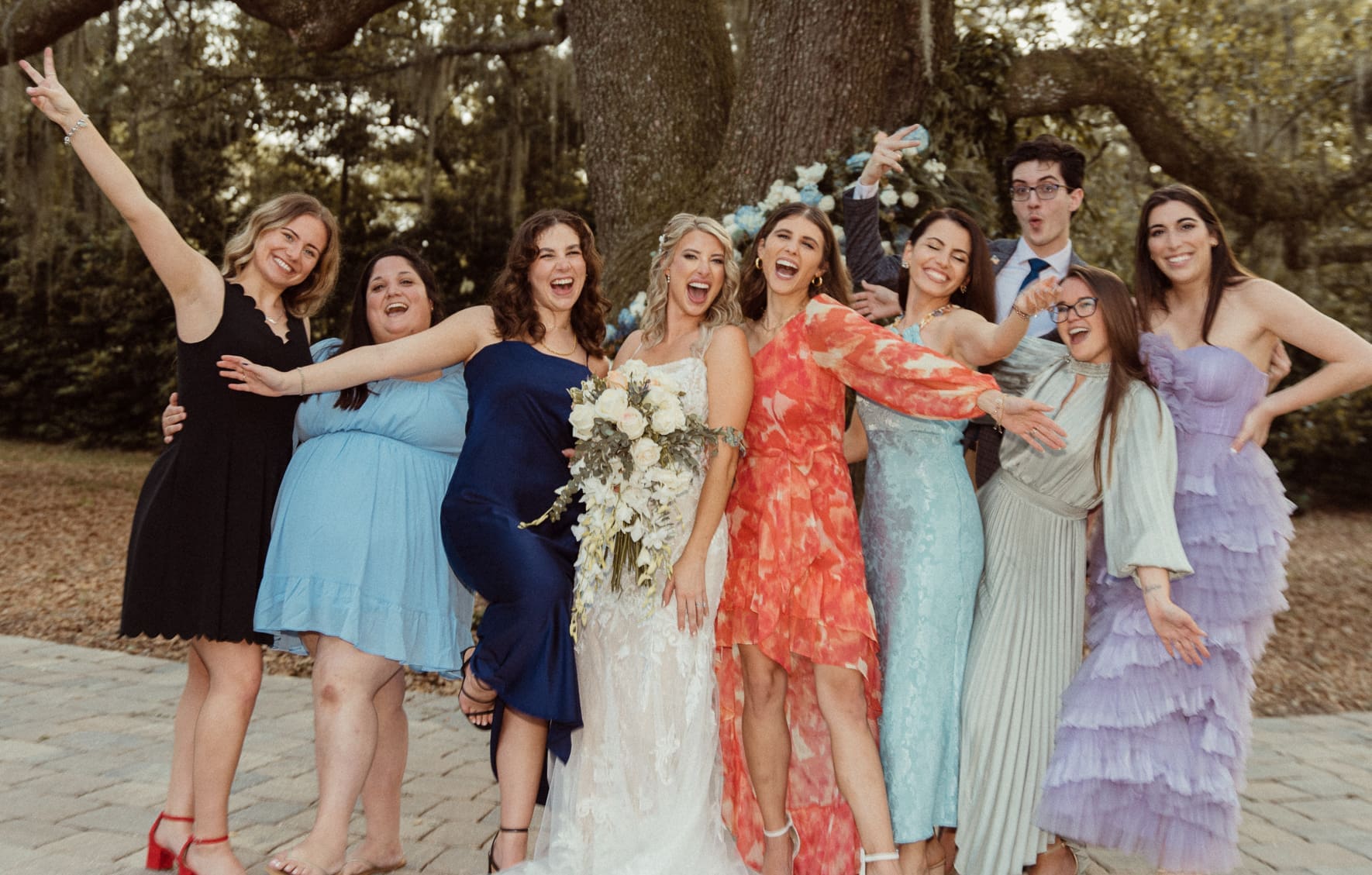 Bride laughing with bridesmaids in colorful dresses under an oak tree at Bowing Oaks wedding. 