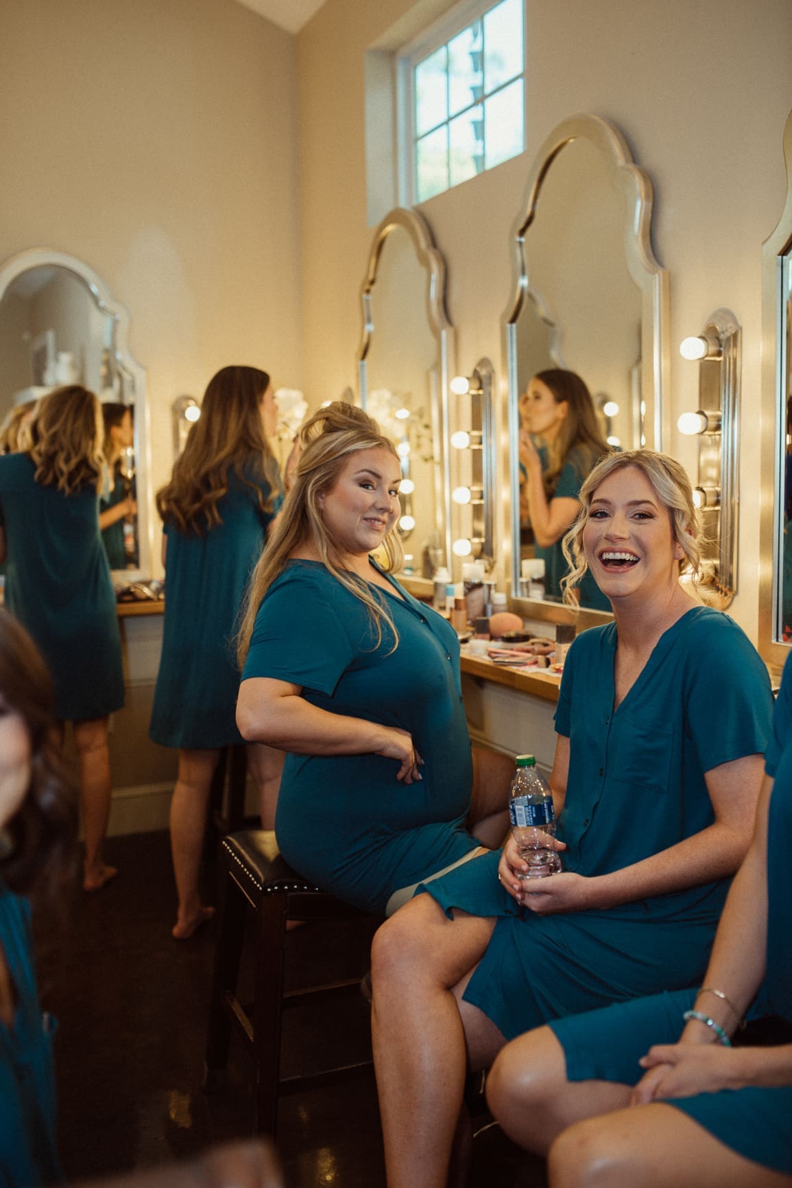 Bridesmaids laughing together at the vanity while getting ready for a Bowing Oaks wedding.