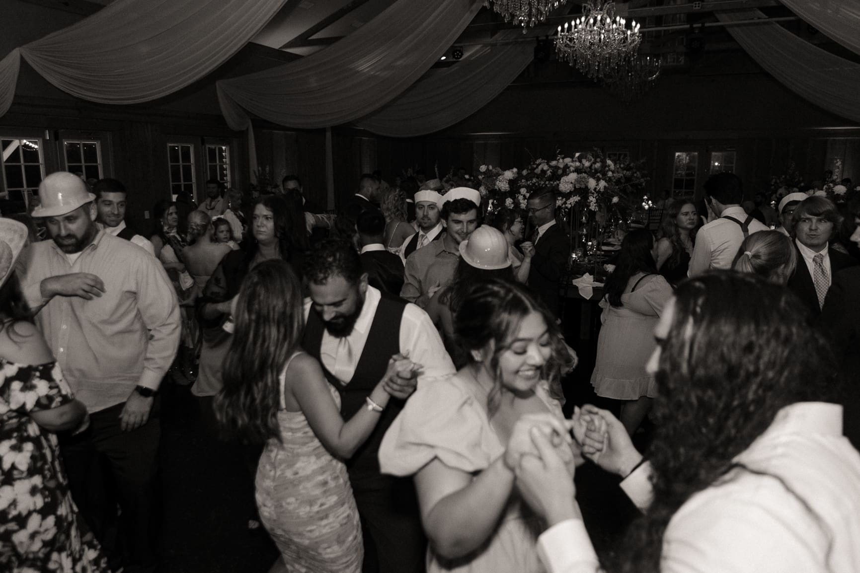 Guests dancing beneath sparking chandeliers on packed dance floor during Bowing Oaks reception.  