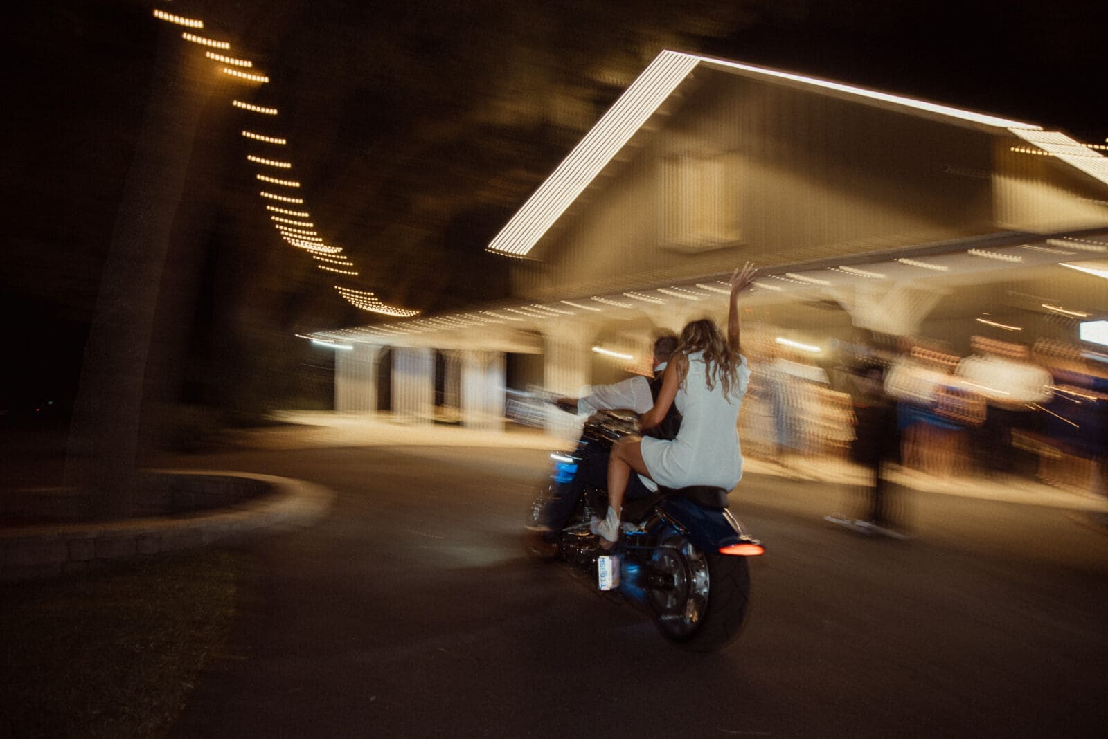 Bride waving goodbye on a motorcycle at night after Bowing Oaks wedding. 