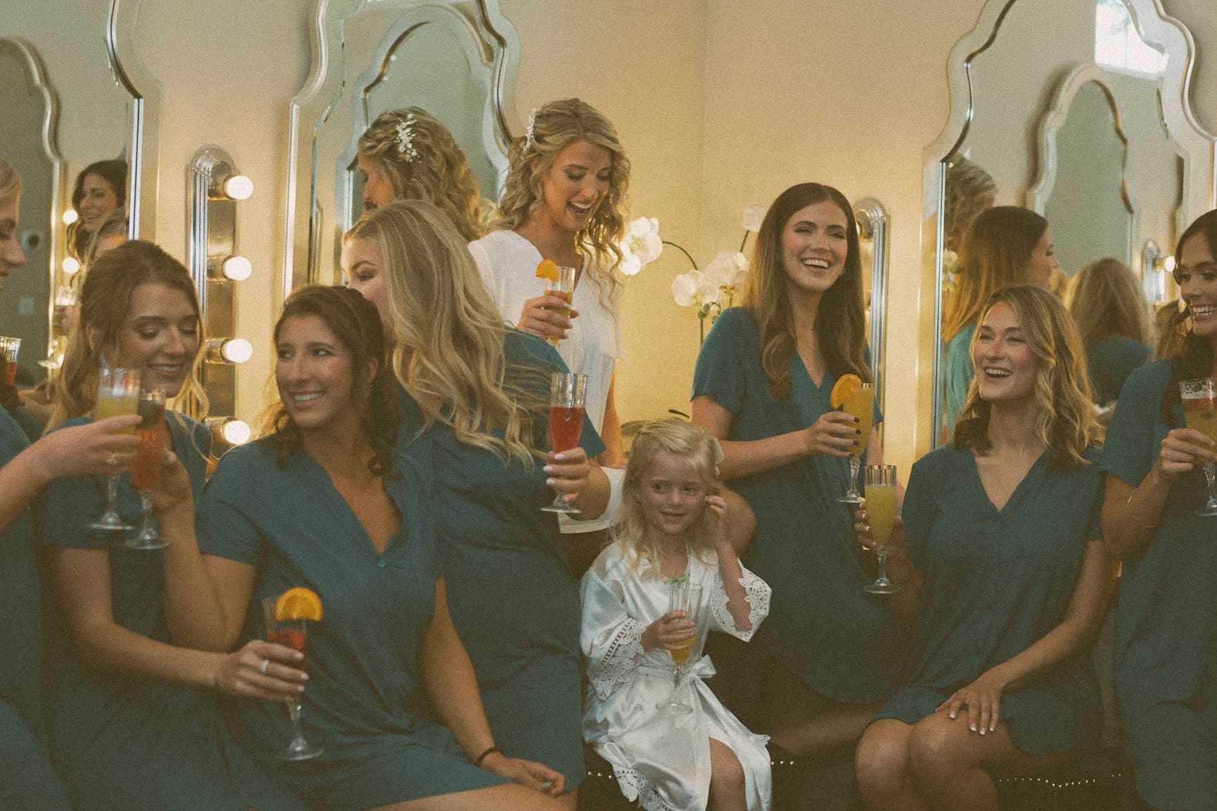 Bridesmaids and flower girl laughing together with drinks before the ceremony. 