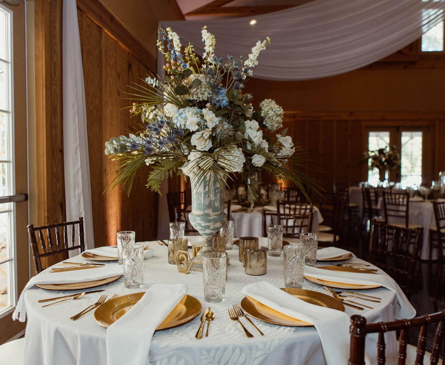 Tall gold and white floral centerpiece on a reception table at Bowing Oaks. 