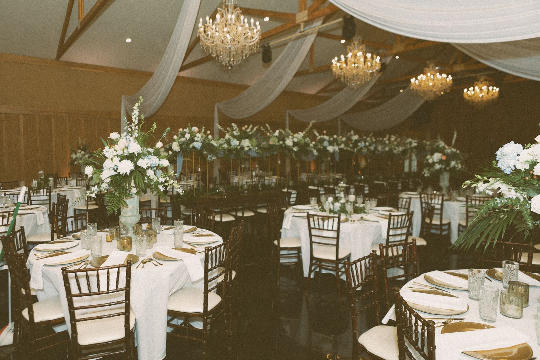 Wide view of the Bowing Oaks reception room set for dinner with chandeliers and floral garland. 