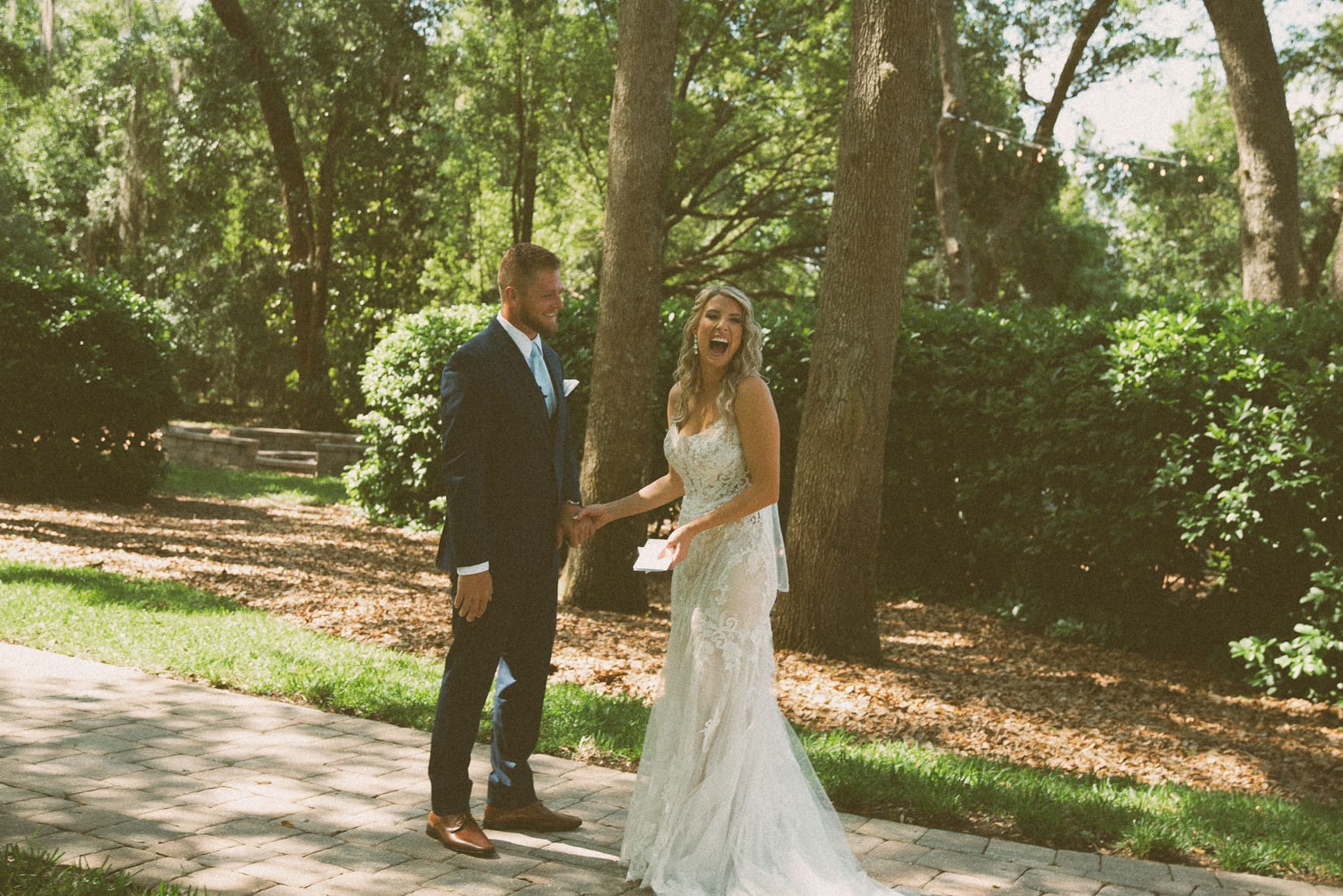Bride laughing candidly while holding hands with groom during first look. 