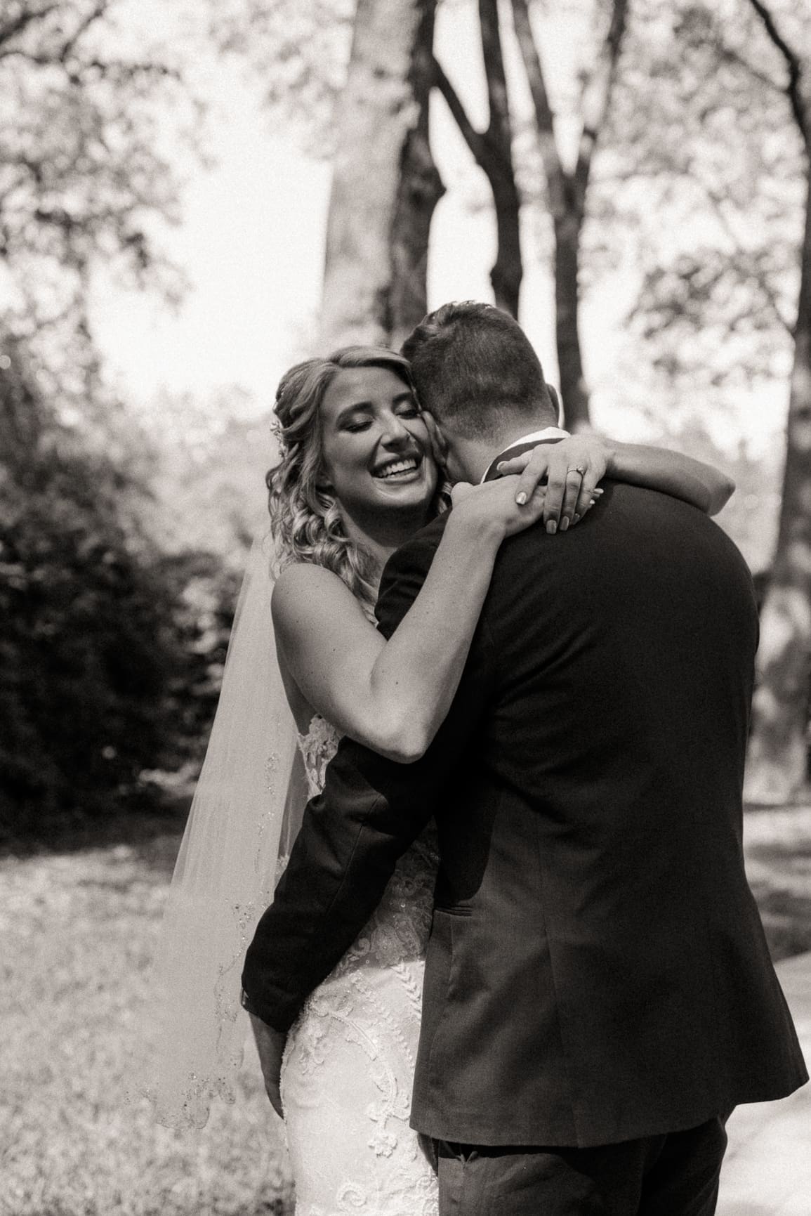 Bride laughing during an embrace with the groom, black and white wedding photo.