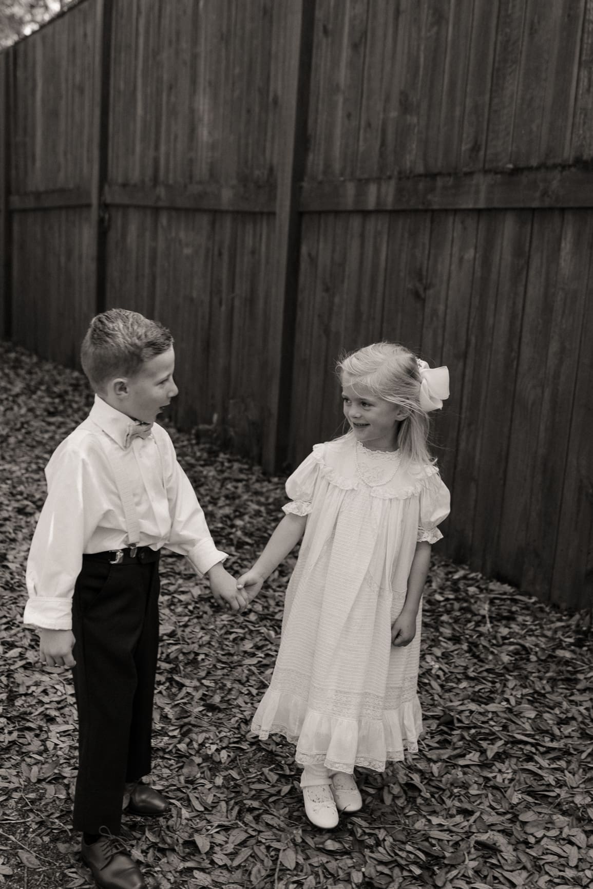 Ringer bearer and flower girl holding hands, black and white wedding photo. 