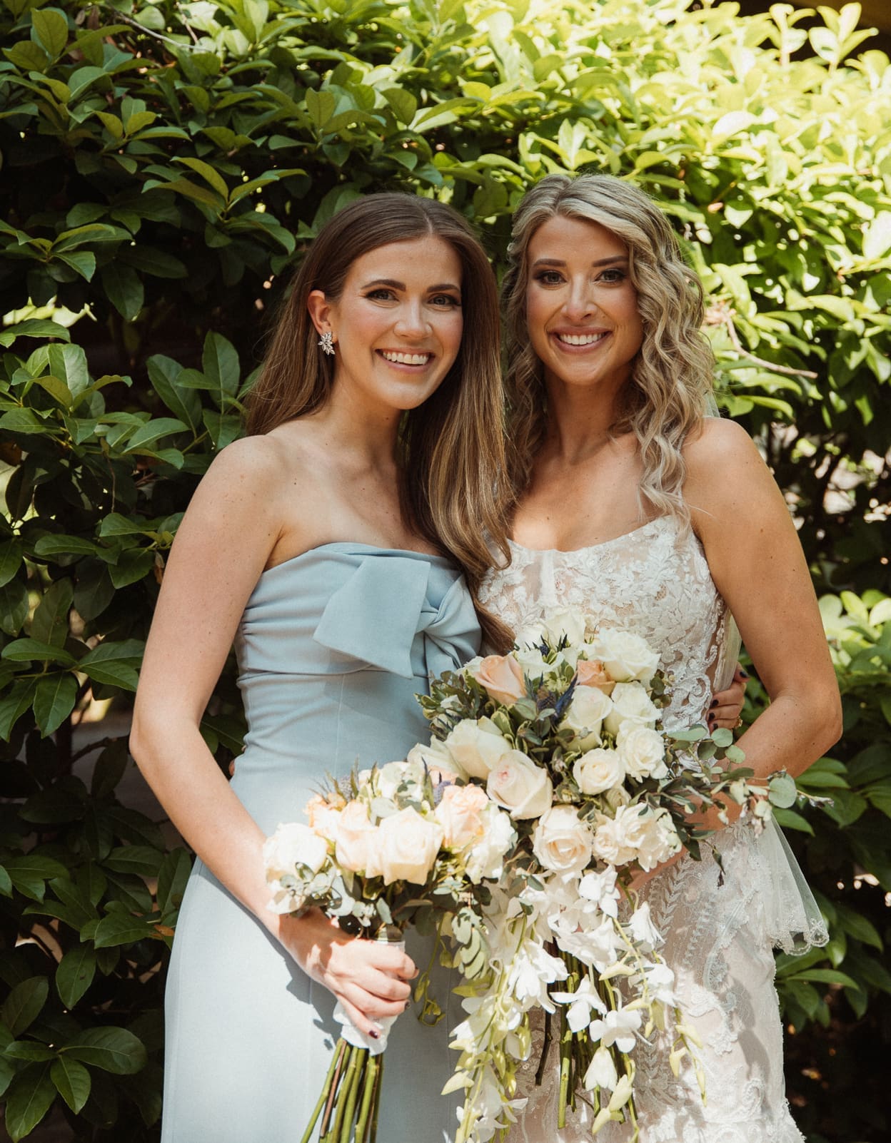 Bride and bridesmaid smiling together holding their bouquets. 