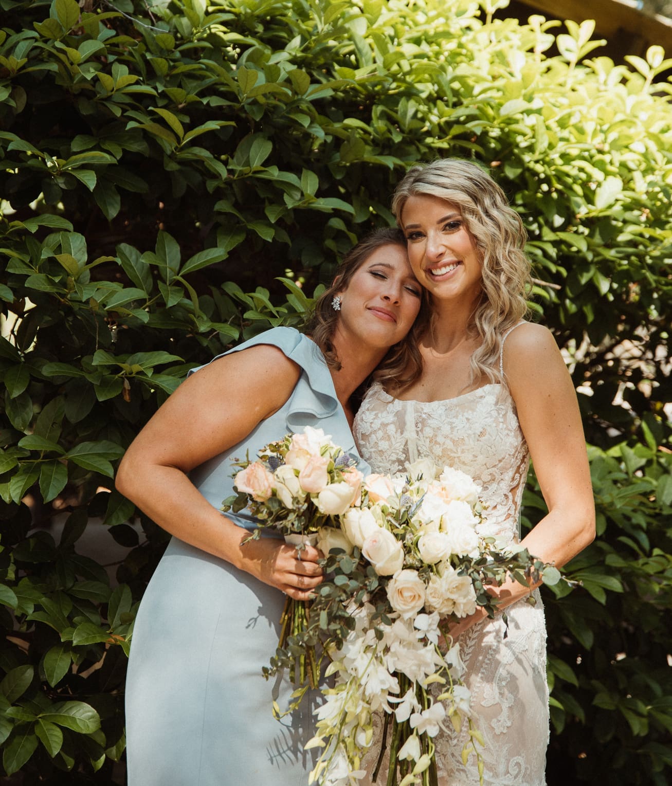 Bride and bridesmaid cheek-to-cheek portrait while holding their bouquets. 