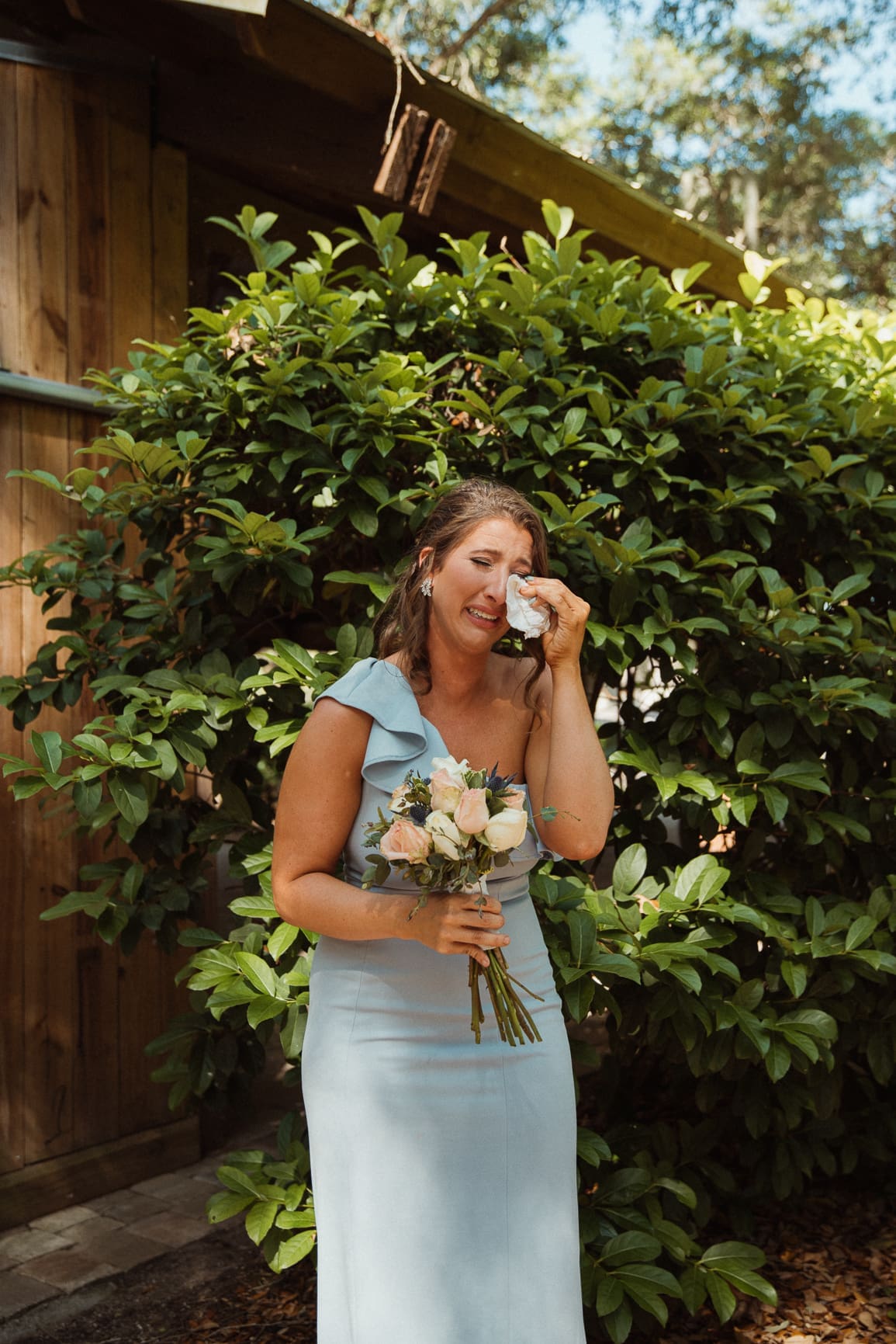 Bridesmaid wiping away tears, emotional moment. 