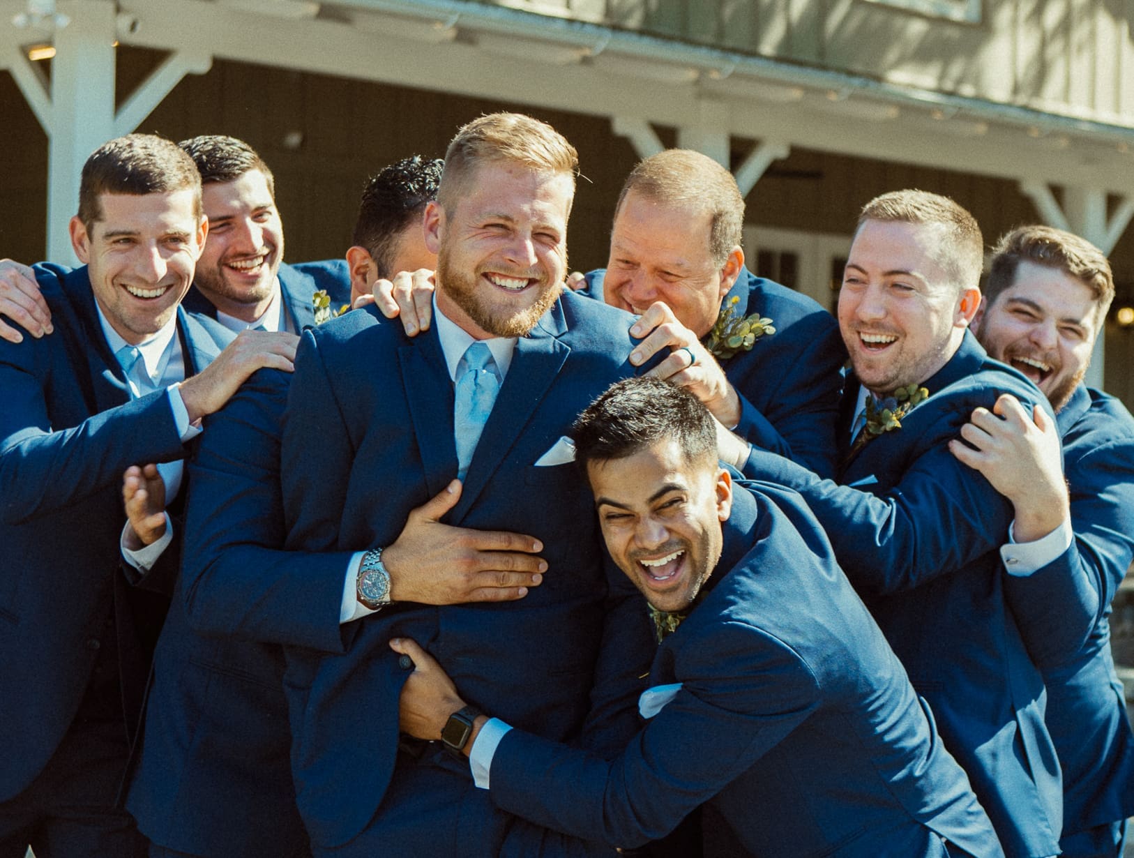 Groomsmen laughing together in a candid group hug before the ceremony. 