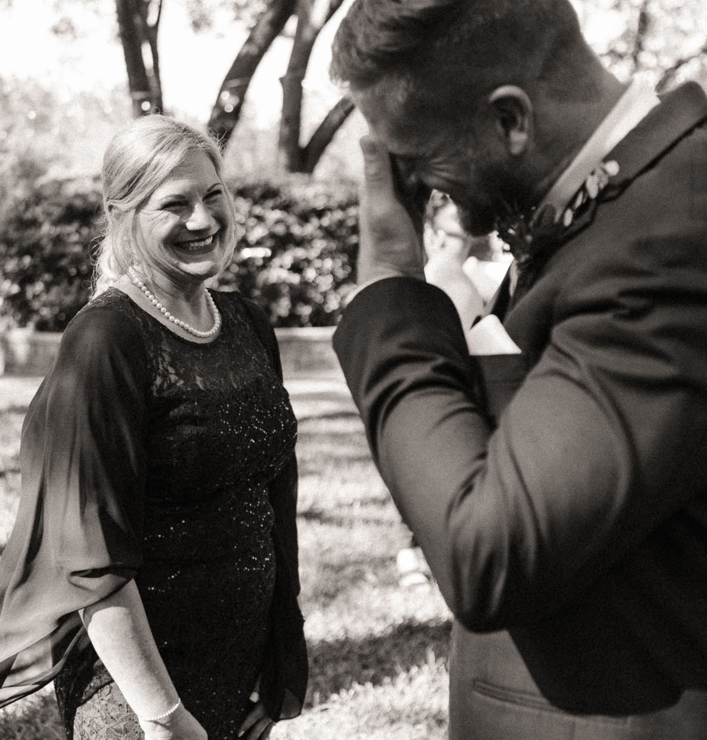 Groom emotional with his mother nearby, black and white wedding photo. 