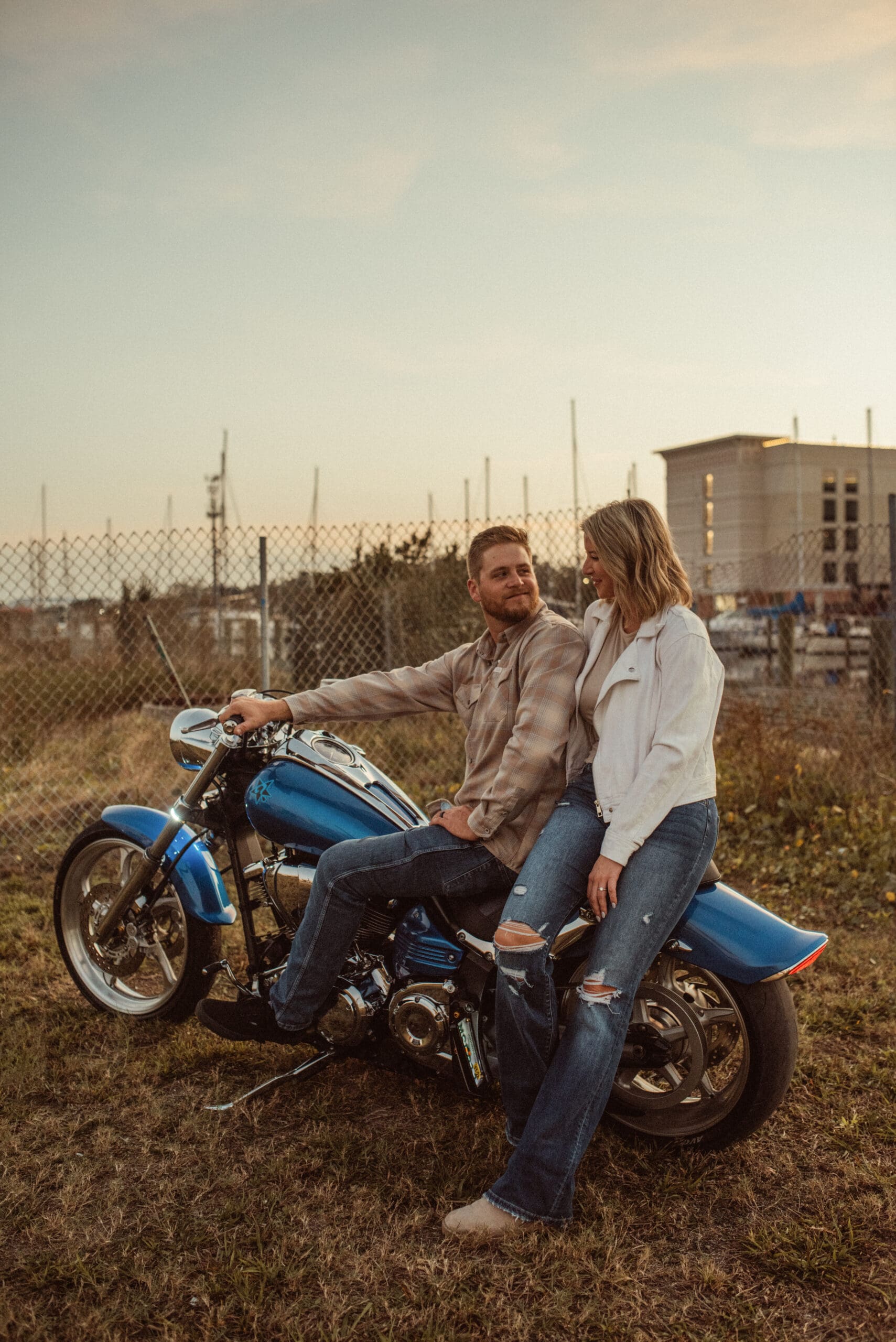 Engaged couple sitting together on a blue motorcycle in an overgrown lot near the St. Augustine marina