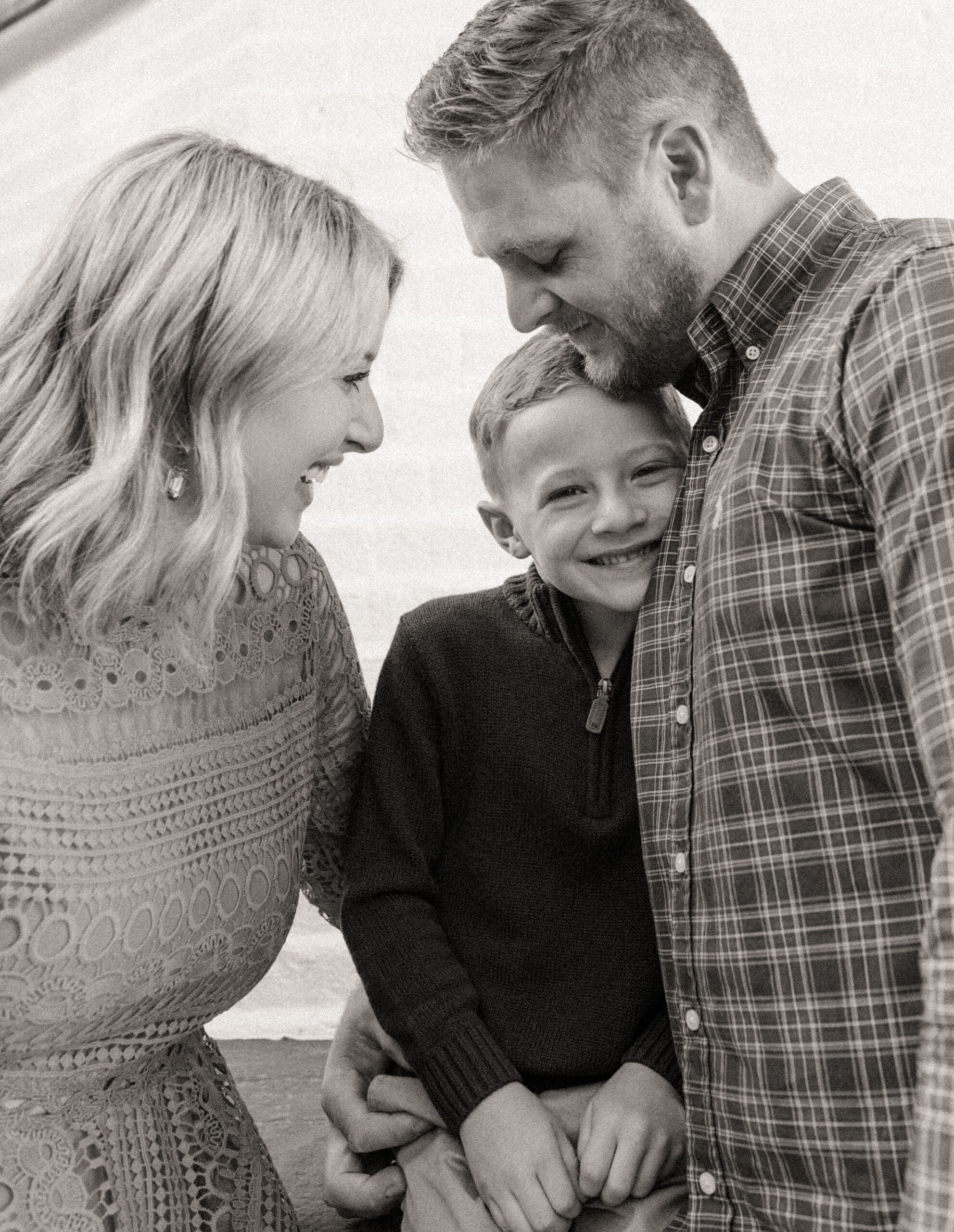  Black and white close-up of a boy smiling between his dad and future stepmom