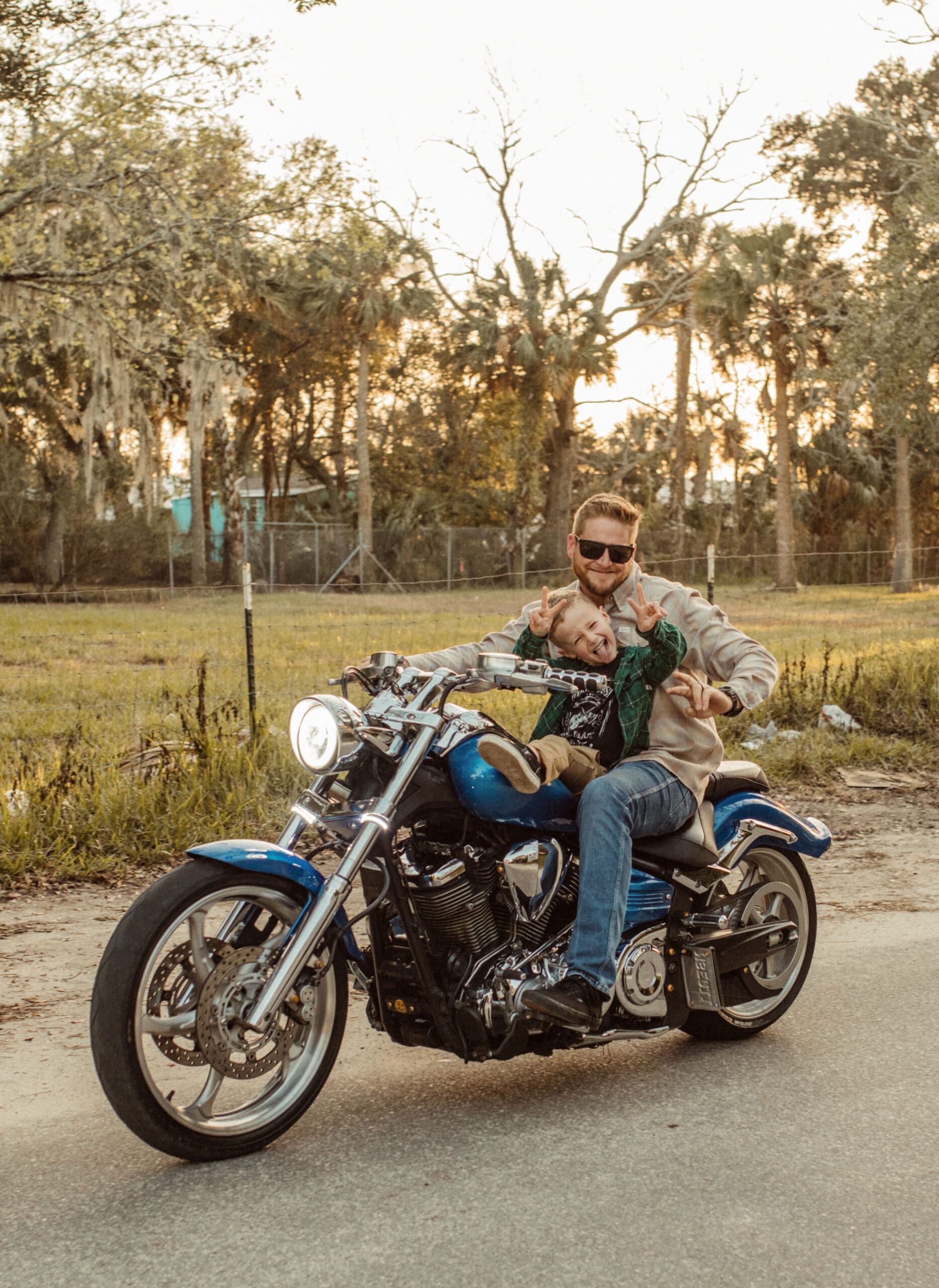 Dad and young son throwing up peace signs on a blue motorcycle during a St. Augustine family engagement session