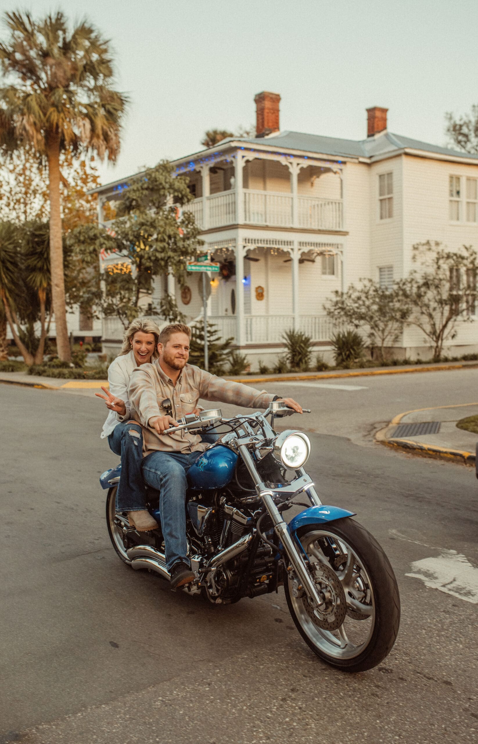 Engaged couple riding a blue motorcycle past a white historic home in downtown St. Augustine