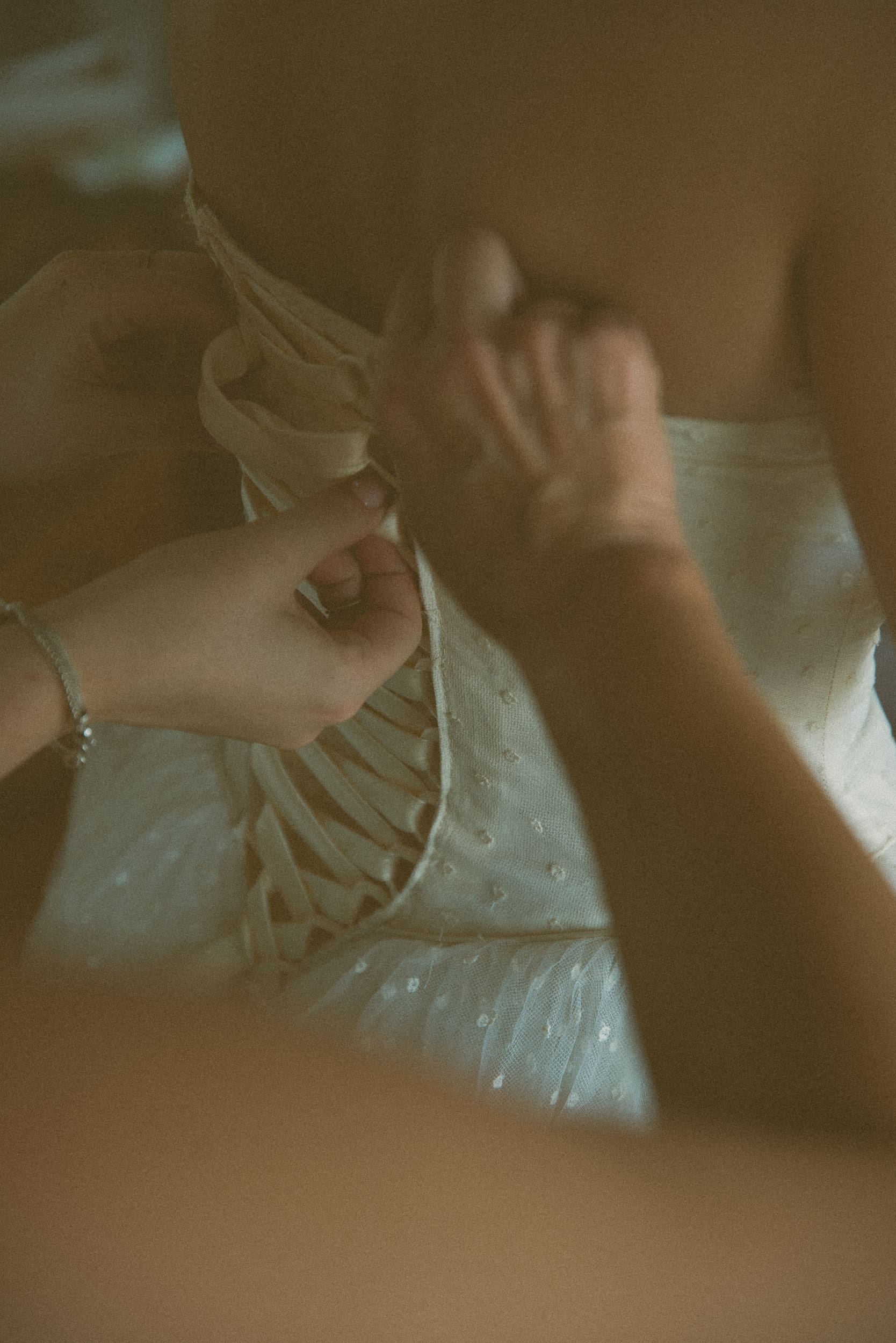 Hands lacing up the back of a bride's corset gown in warm, grainy film tones.