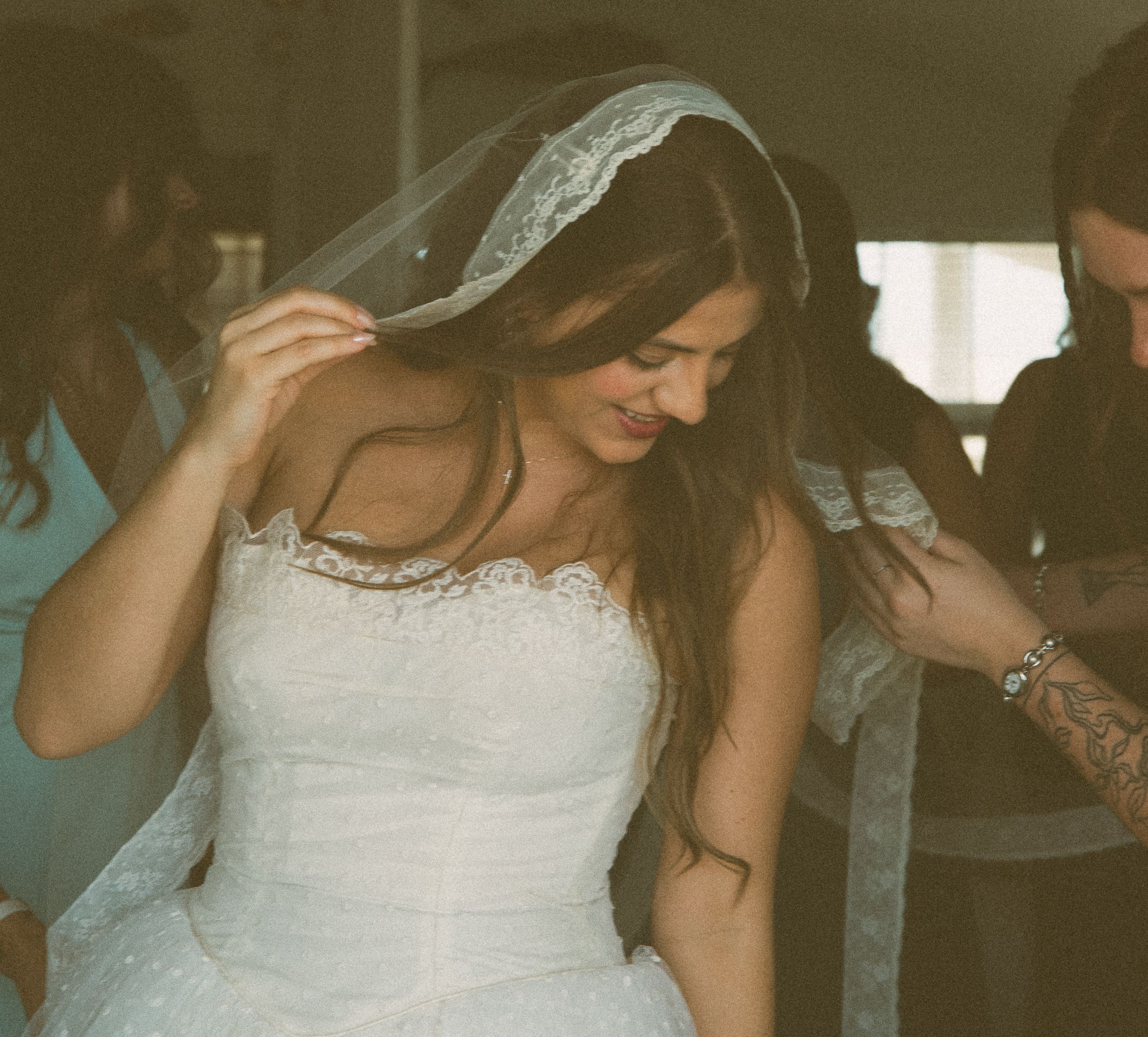  Bride laughing and looking down as her lace veil is placed, in warm film tones.