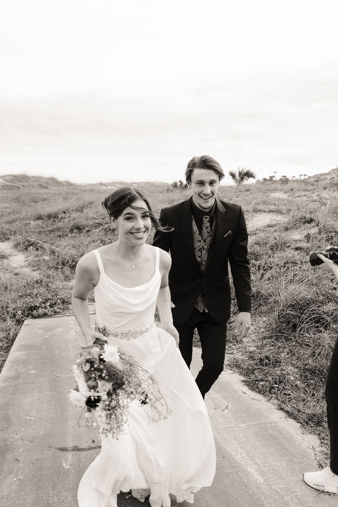 Couple walking through coastal dunes, laughing, on black and white film.