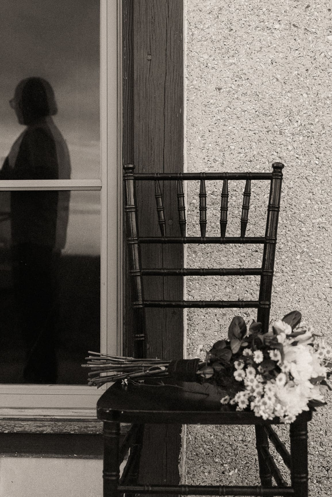Bouquet resting on a chiavari chair beside a window silhouette, on black and white film.