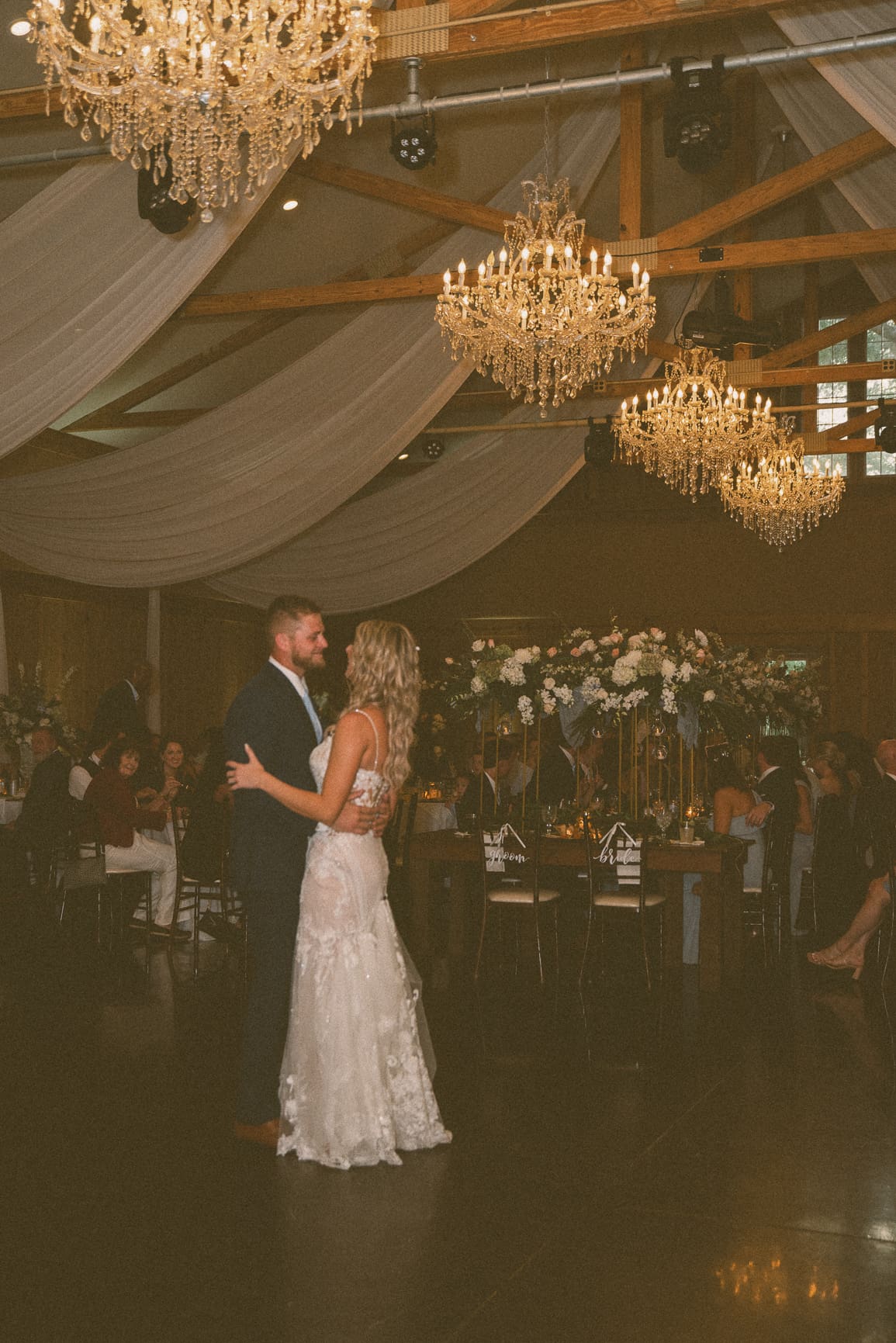 Couple sharing their first dance beneath crystal chandeliers and draped fabric, captured on color film.