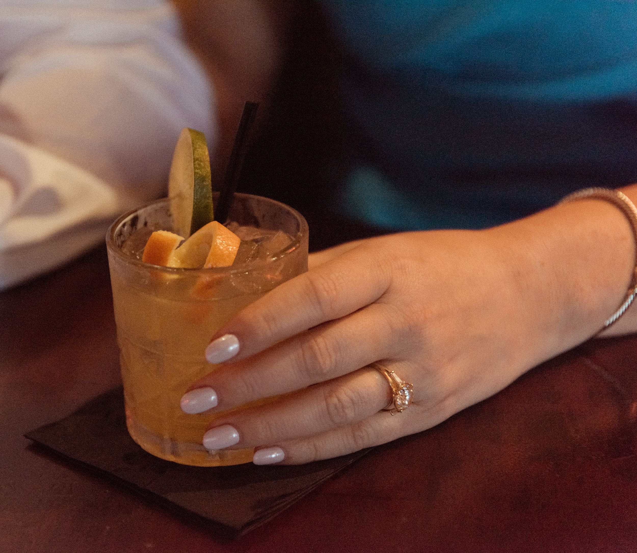 Close-up of an engagement ring on a hand holding a citrus cocktail