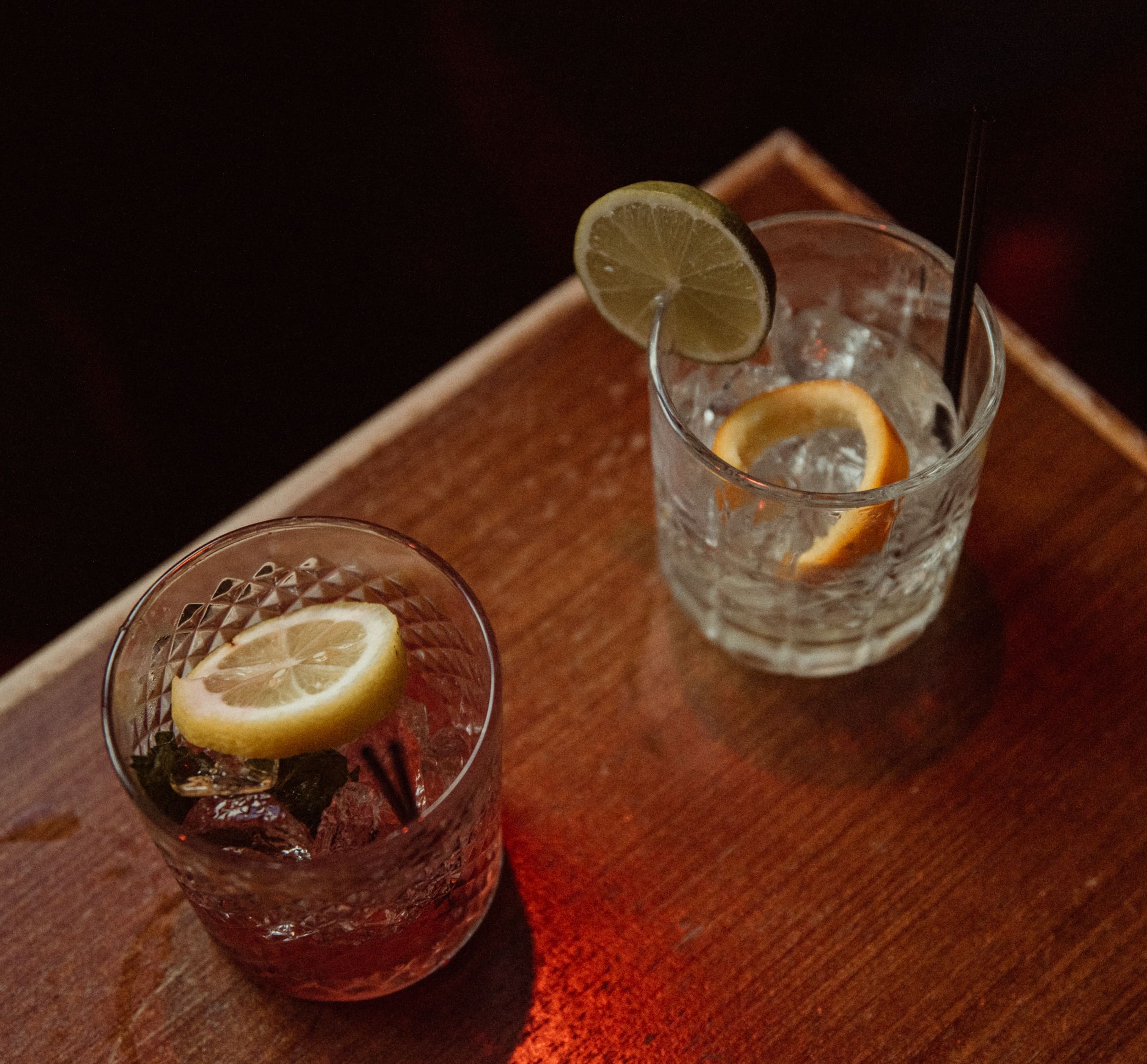 Overhead view of two cocktails with lemon and lime garnishes on a wooden table at Dos Gatos