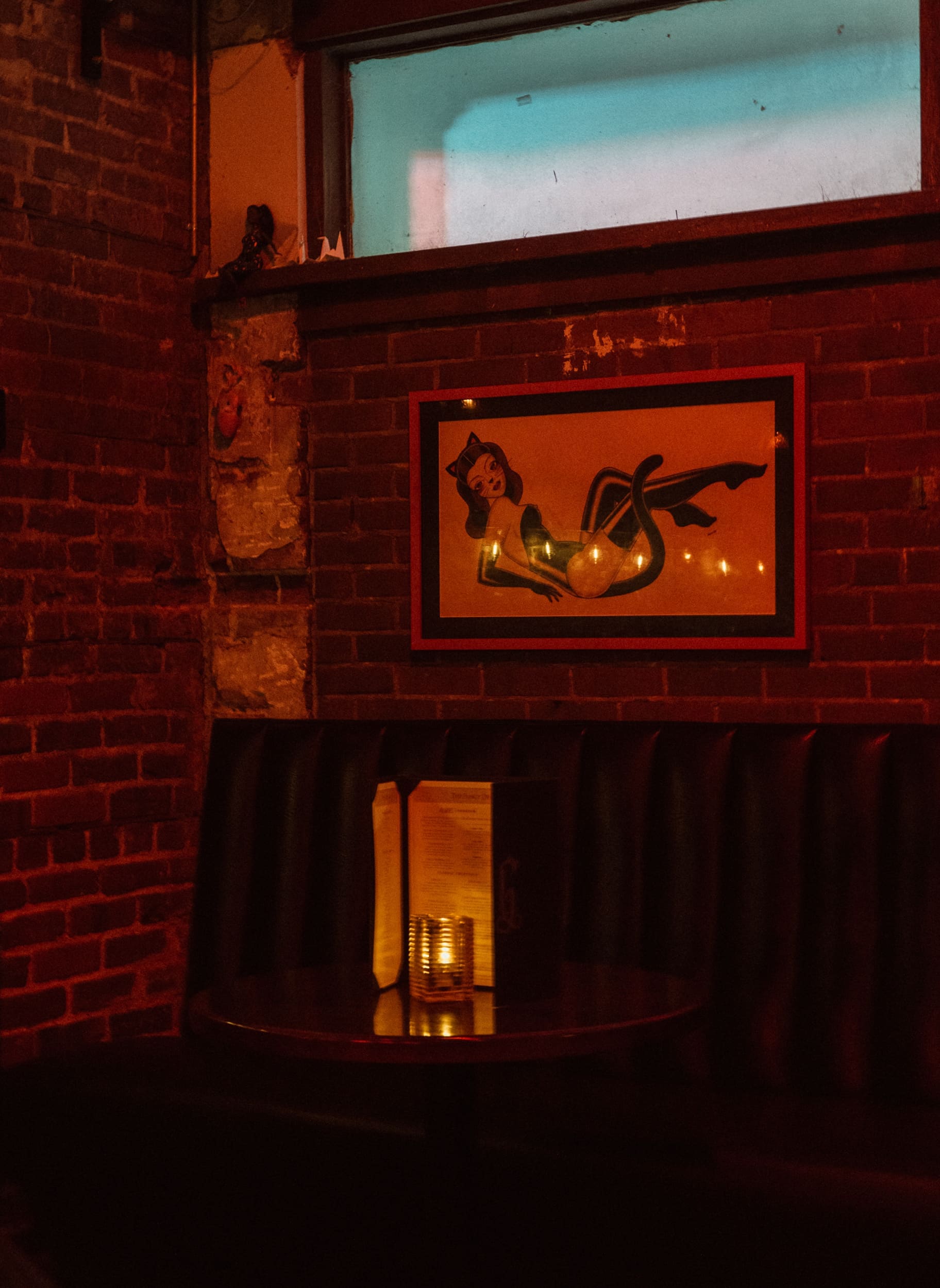 Pin-up art print on an exposed brick wall glowing in red light at Dos Gatos