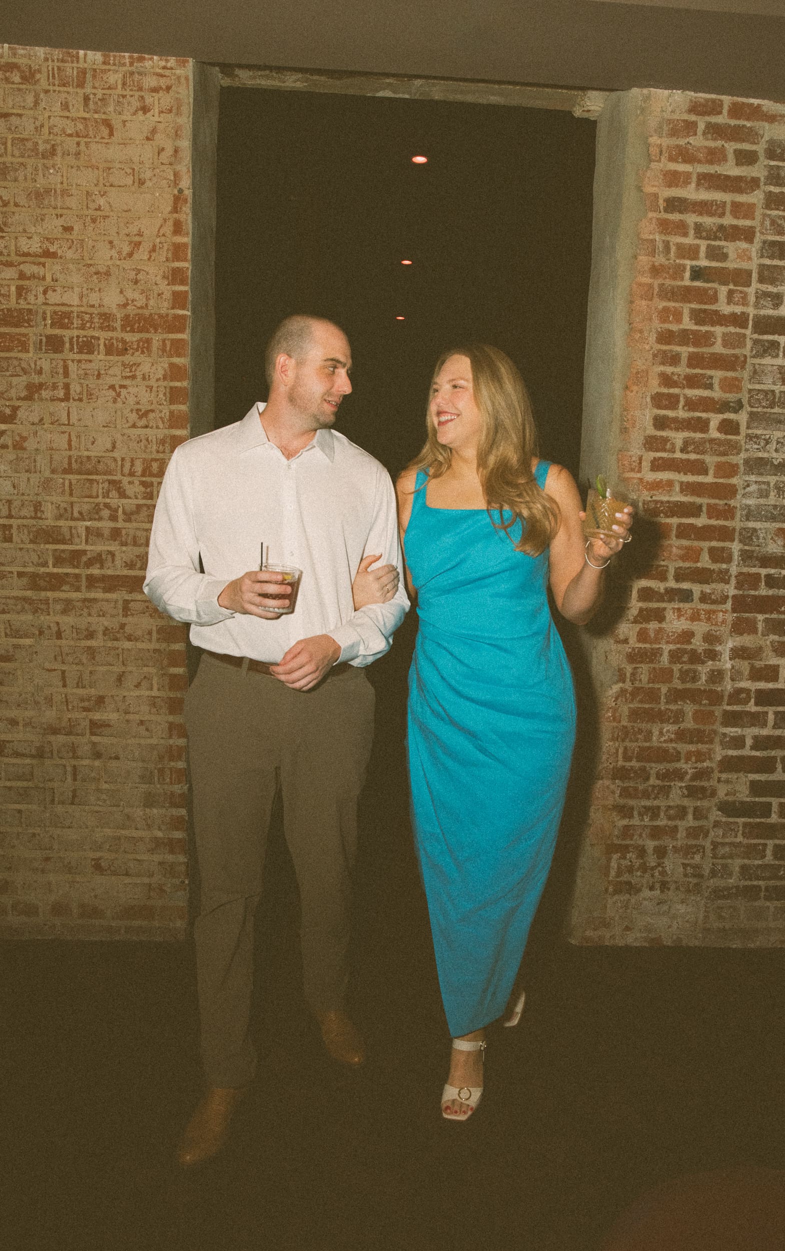 Couple walking arm in arm with cocktails through a brick doorway at Dos Gatos in downtown Jacksonville